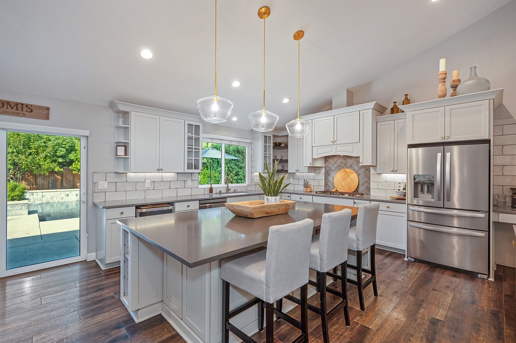 Remodeled kitchen with a large gray island, white cabinets, stainless appliances, and sliding doors to the pool patio.