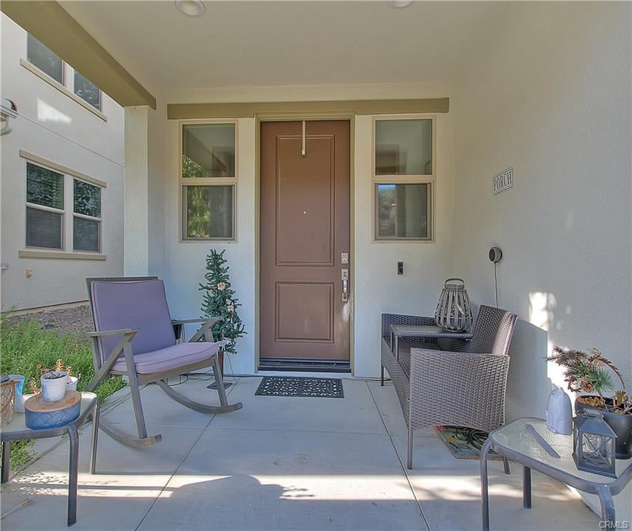 Covered porch with a brown front door, windows, and seating.