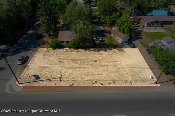Cleared vacant lot outlined in red at a street corner, surrounded by homes and trees.