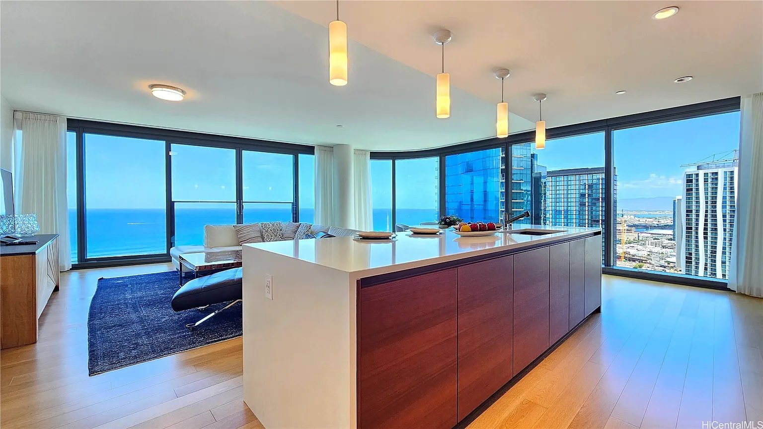 Open-plan condo kitchen with a large wood island and floor-to-ceiling windows overlooking the ocean and city.