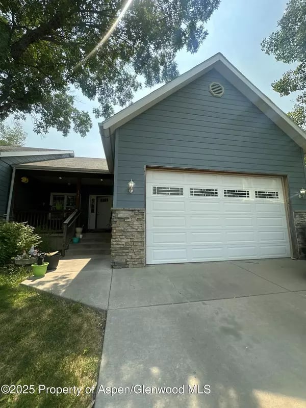 Blue-gray house with a white double garage door, stone accents, and a shaded front porch.