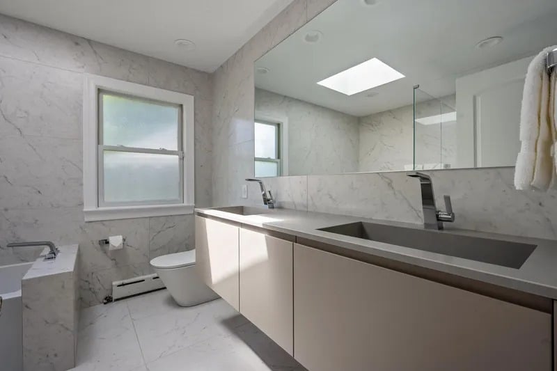 Modern marble bathroom with floating double vanity, large mirror, and window.
