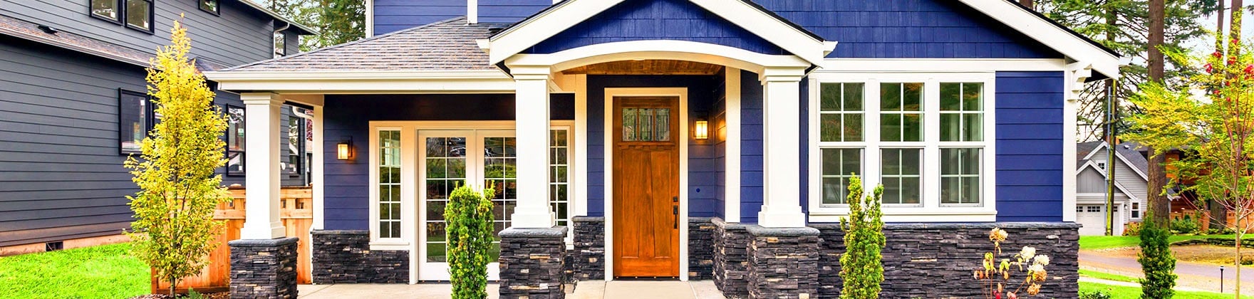 Blue house with white trim, stone porch pillars, and a wooden front door.