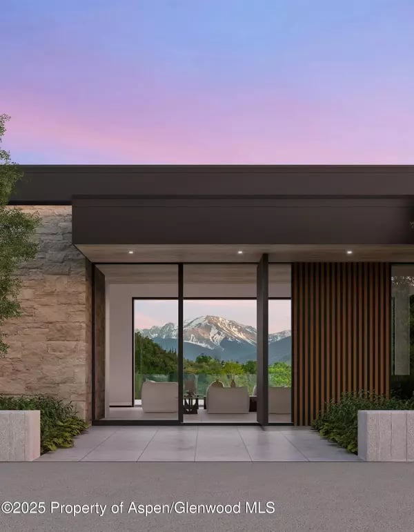 Modern Aspen home entrance with stone facade, glass doors, and mountain views at dusk.