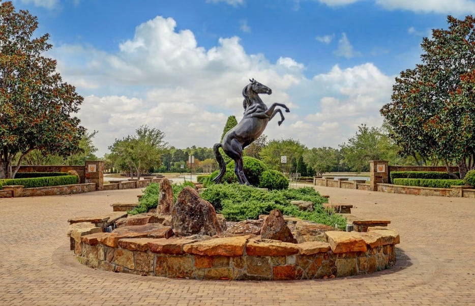 A rearing horse statue stands in a landscaped plaza surrounded by stonework and trees.