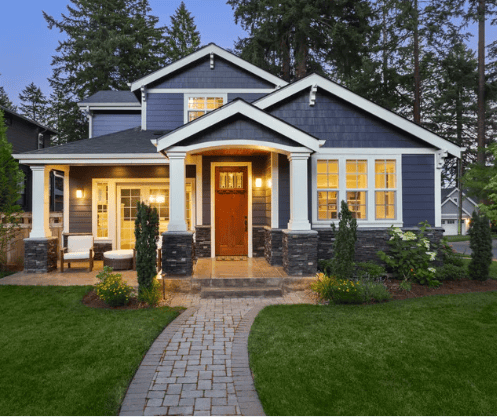 Blue-gray home with a covered porch, warm window lights, and a curved stone walkway.