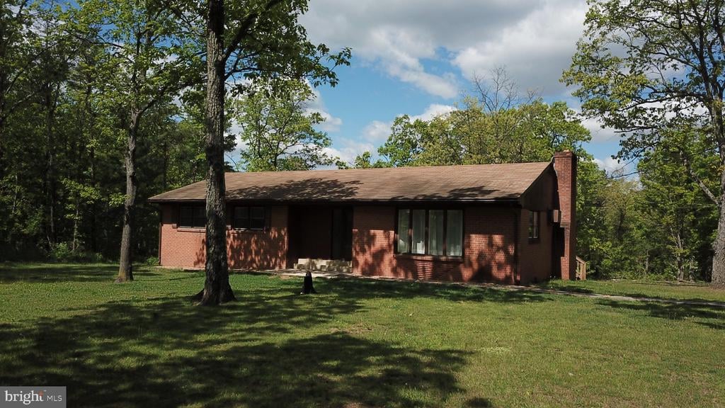 Single-story red brick house with a chimney, surrounded by mature trees and a broad lawn.