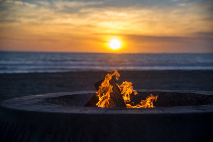 Fire pit bonfire burning on sandy beach at ocean sunset