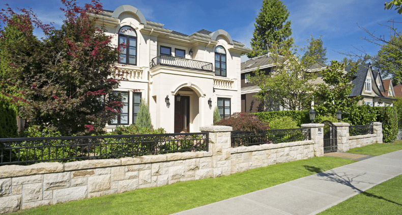 White two-story house with arched windows and a balcony behind a stone wall.