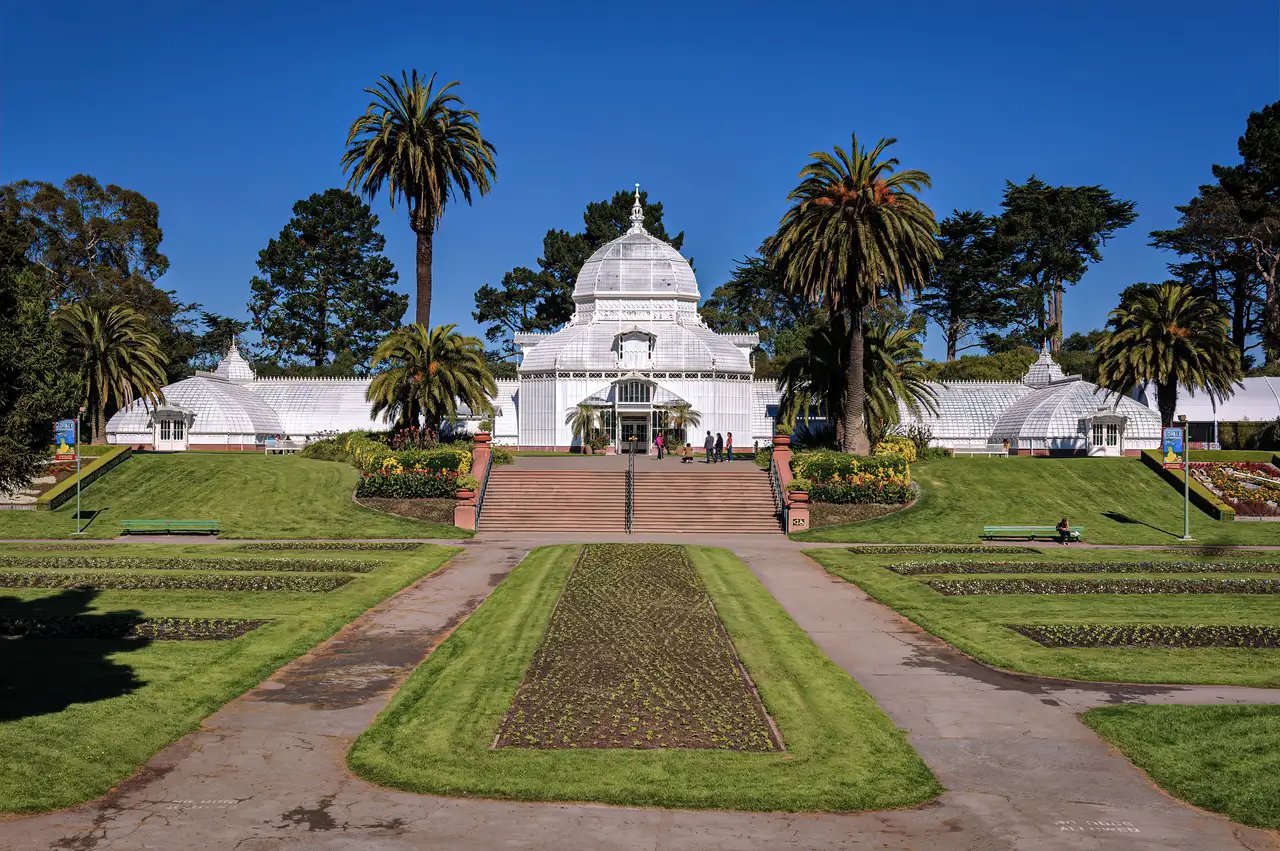 Exterior view of the Conservatory of Flowers showing its Victorian white architecture against the backdrop of Golden Gate Park's lush greenery