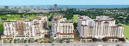 Aerial view of condominium buildings with green grounds, cityscape, and ocean in the distance.