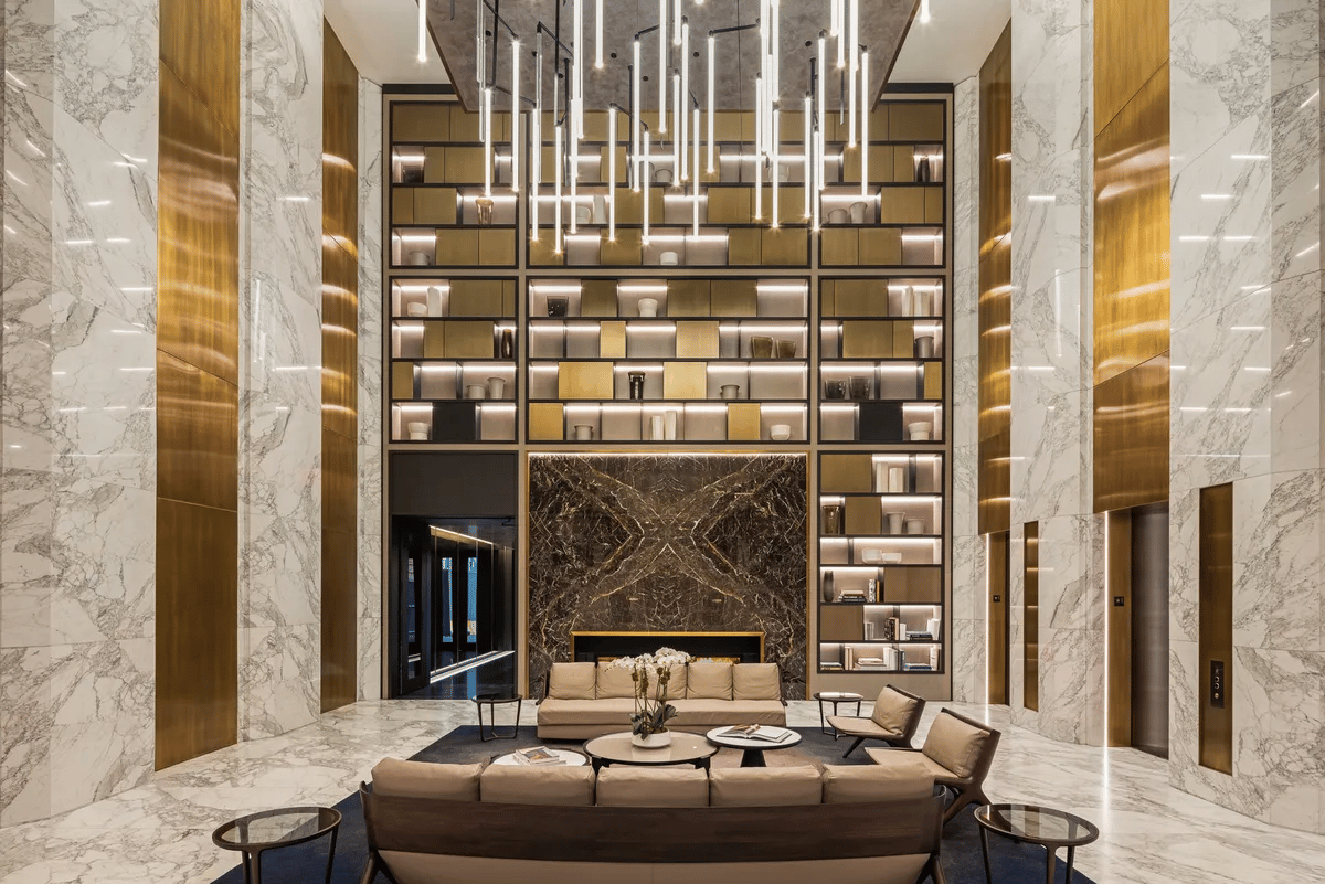 Lobby with marble walls, brass panels, illuminated shelves, and lounge seating.