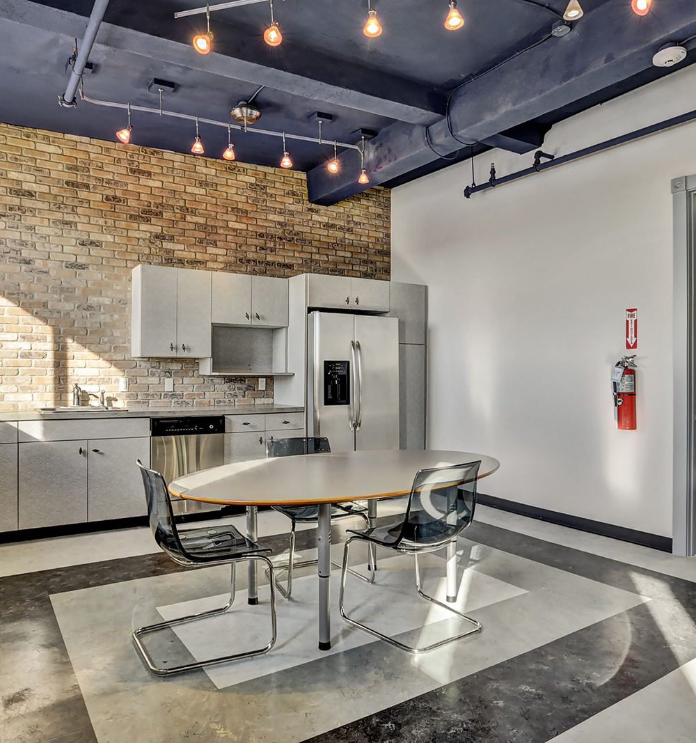 Kitchen and dining area with a brick backsplash, stainless appliances, and an oval table beneath pendant lights.