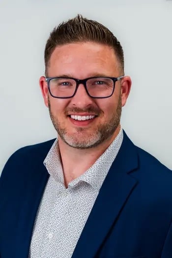 Matt Meyer smiling in glasses, wearing a navy blazer and patterned white shirt.
