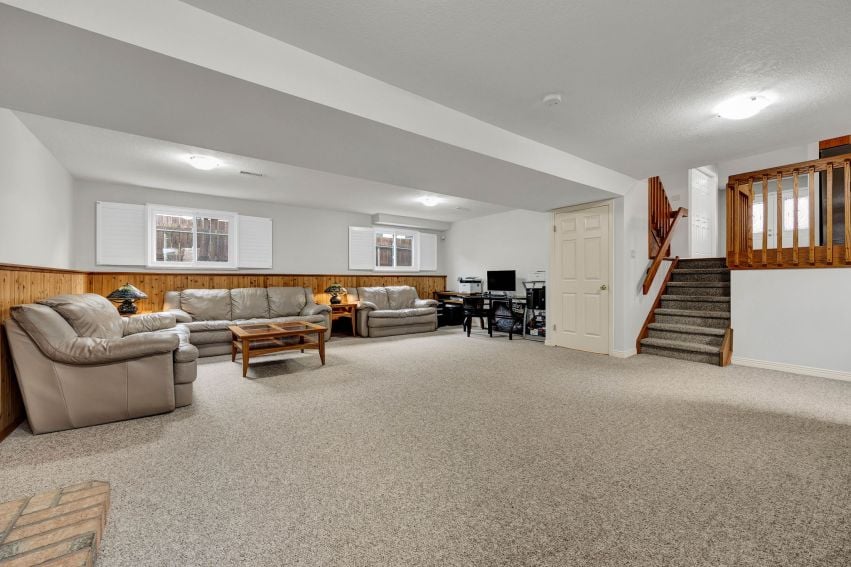 Living room with beige carpet, leather sofas, and a staircase to the upper level.