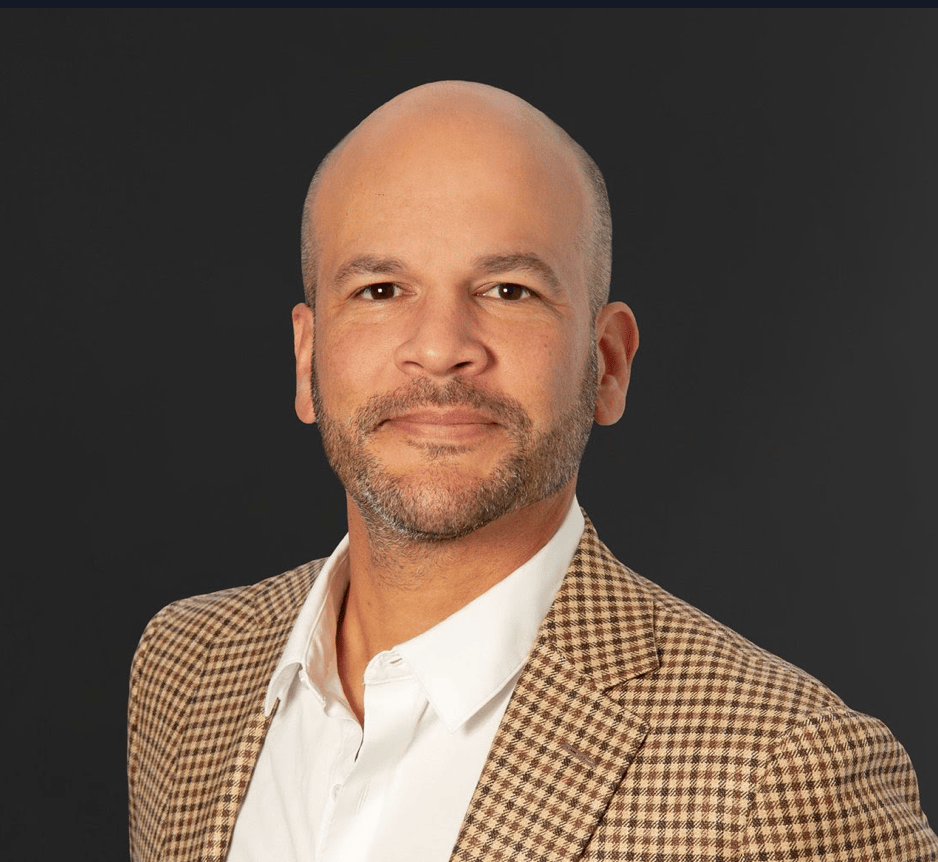 Man in a brown checked blazer and white shirt.
