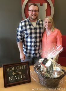 Colin and Ashley pose beside a Bialik Real Estate sign and gift basket.