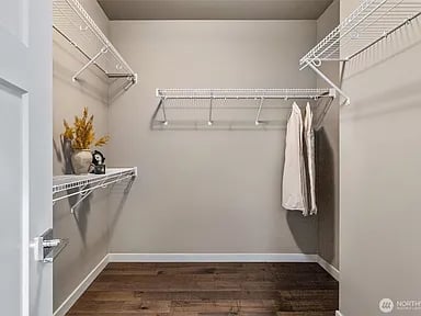 Walk-in closet with white wire shelving, a few hanging garments, and dark wood flooring.