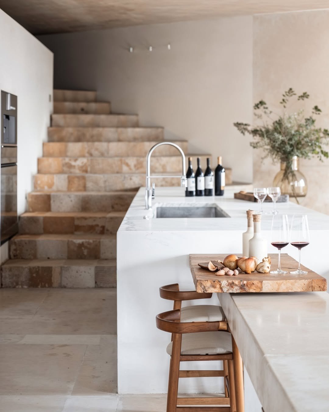 Luxury minimalist kitchen interior with a marble island, warm wood accents, wine glasses, and natural décor, reflecting the editorial marketing style of Amy Ali Agency West.