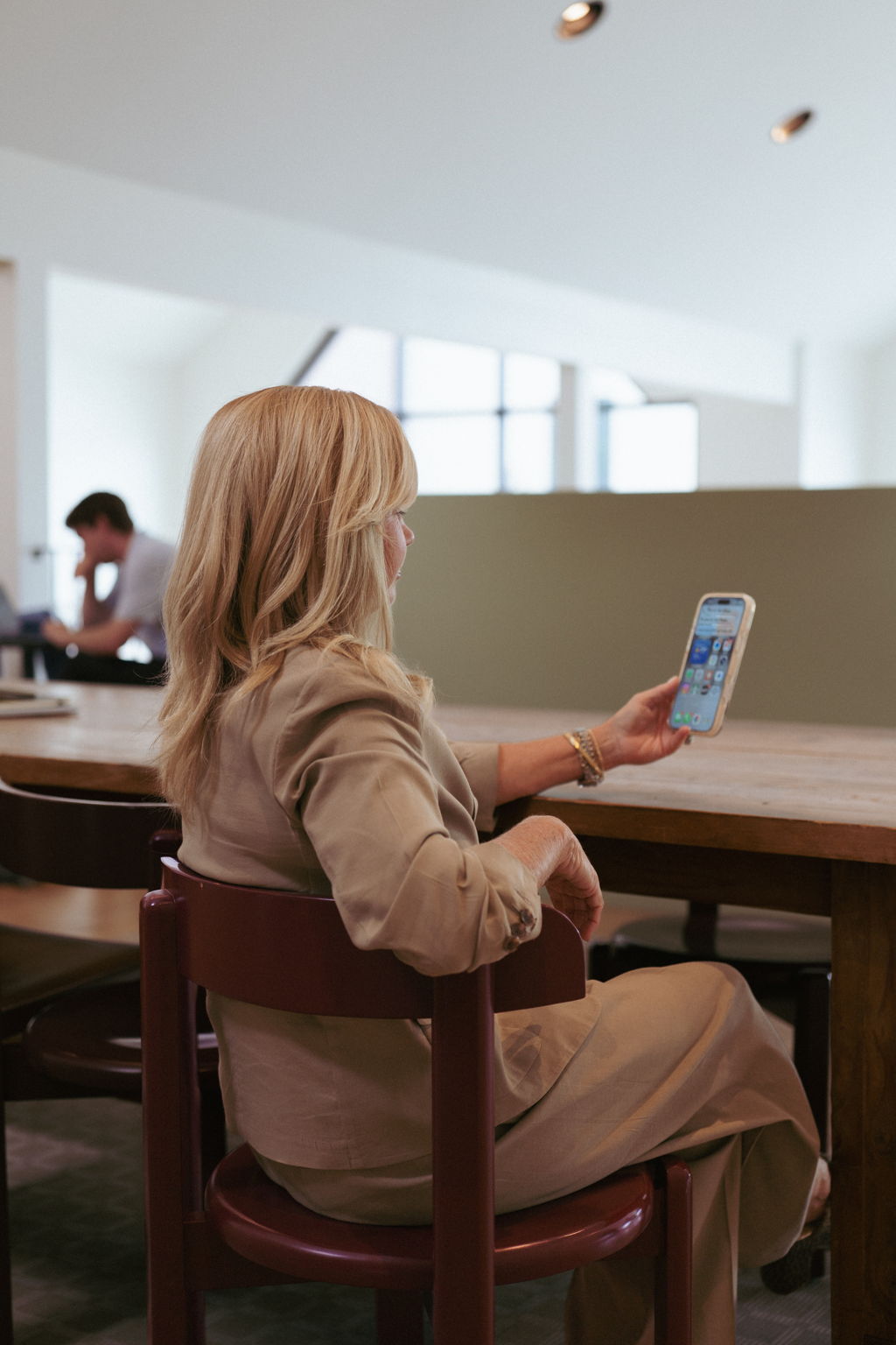 A woman seated at a wooden counter looks at her smartphone in a bright office.