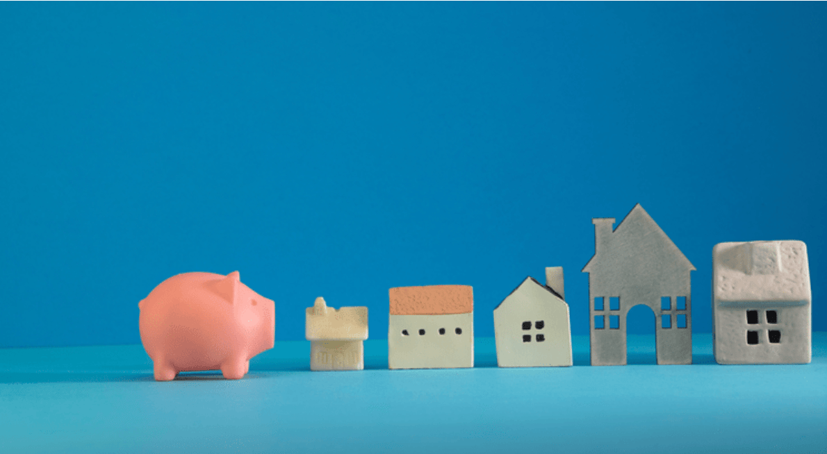 A pink piggy bank beside a row of miniature houses.