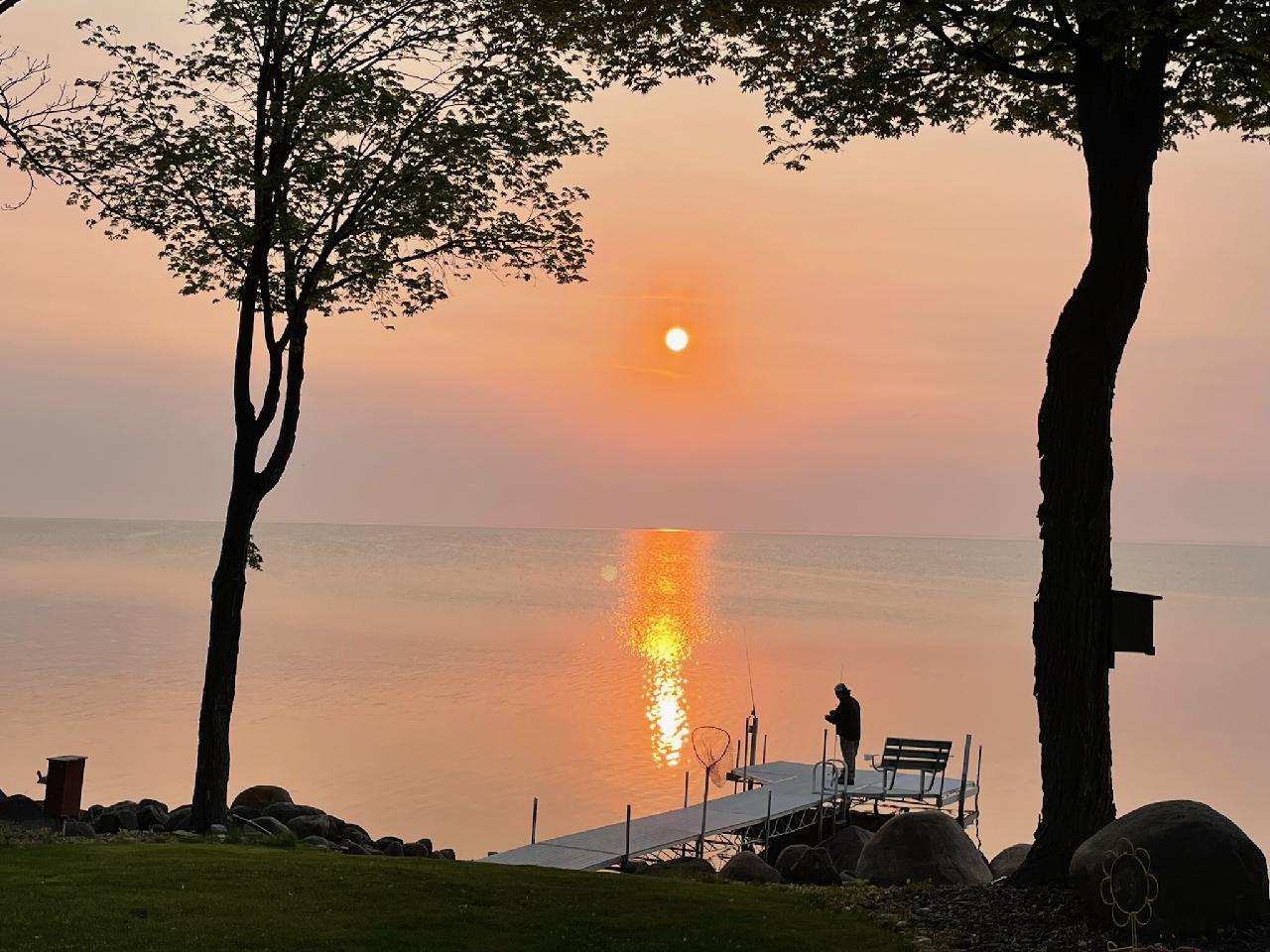 A lakeside dock at sunset, with sunlight reflecting across calm water between shore trees.