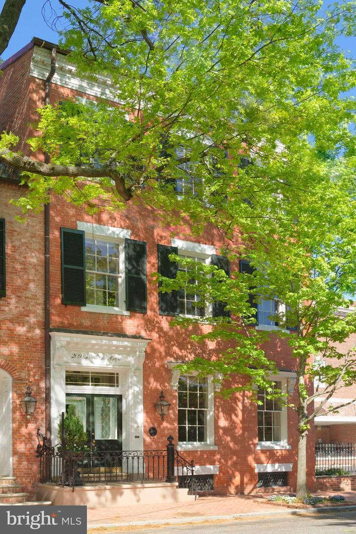 Red-brick townhouse with black shutters and a leafy tree shading the facade.