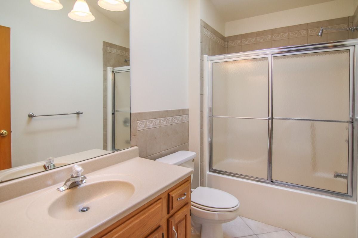 Bathroom with a tan vanity and bathtub behind frosted sliding glass doors.