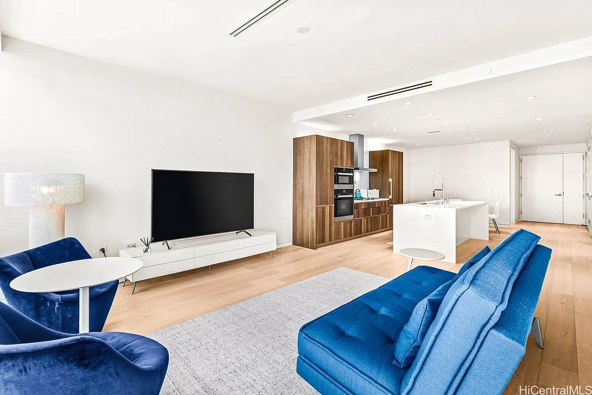 Living room with blue seating, a white media console, and an open kitchen with walnut cabinetry.