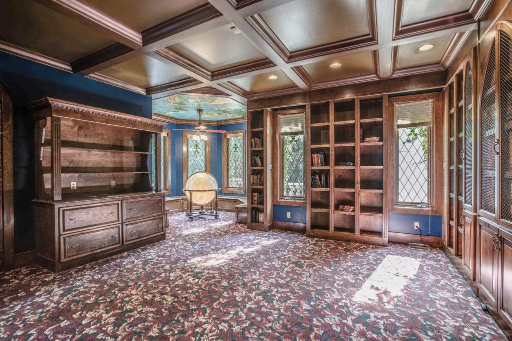 Wood-paneled library with built-in bookcases, leaded-glass windows, a coffered ceiling, and a globe.