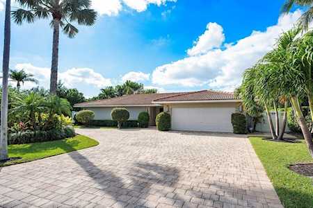 Single-story home with a wide paved driveway, two-car garage, and tropical landscaping.