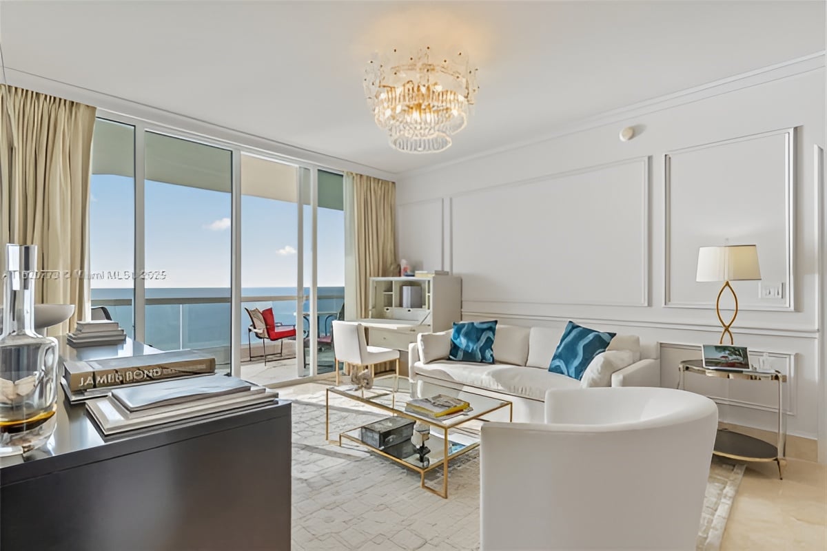 Furnished living room with ocean-view balcony, white seating, and crystal chandelier.