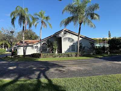 Single-story home with arched windows, a dark gabled roof, and tall palm trees along the front lawn.