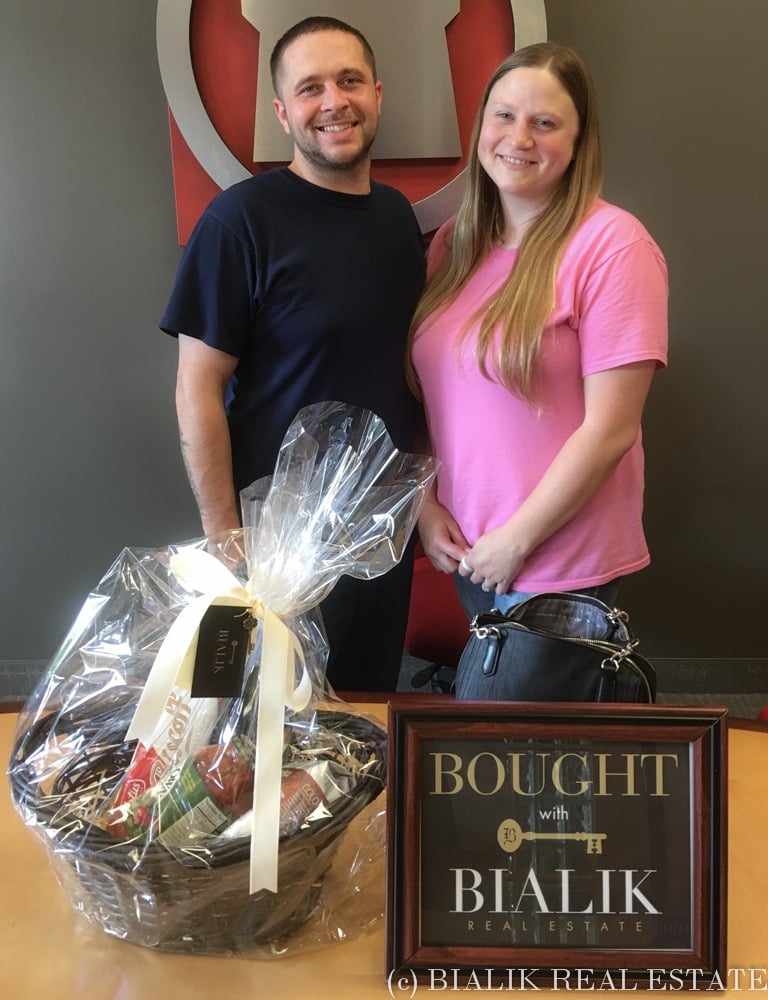 Brandon and Heather pose with a gift basket and framed Bialik Real Estate sign.