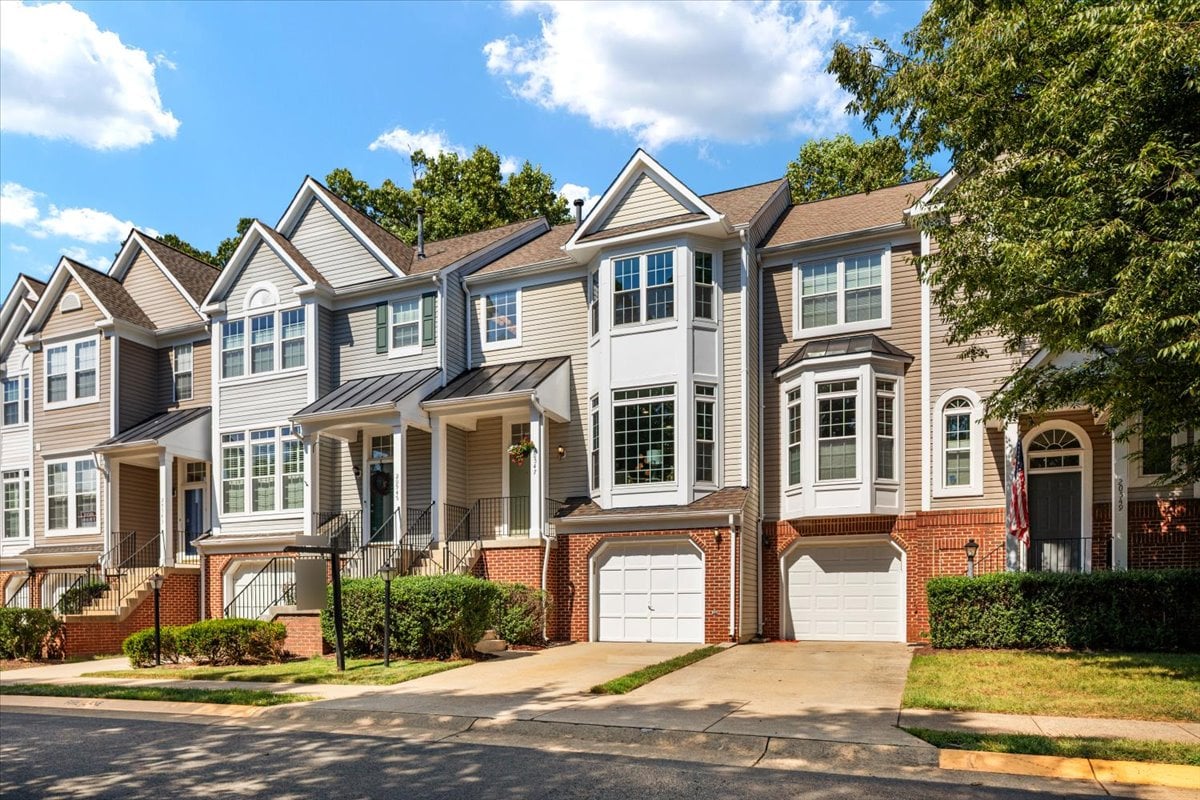 Attached townhouse with light siding, brick lower level, bay windows, and an attached garage.
