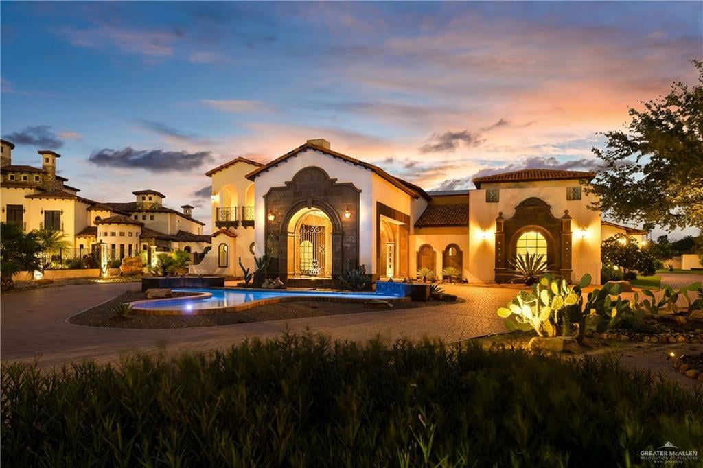 Luxury Mediterranean-style home at dusk with an arched stone entrance and illuminated pool.