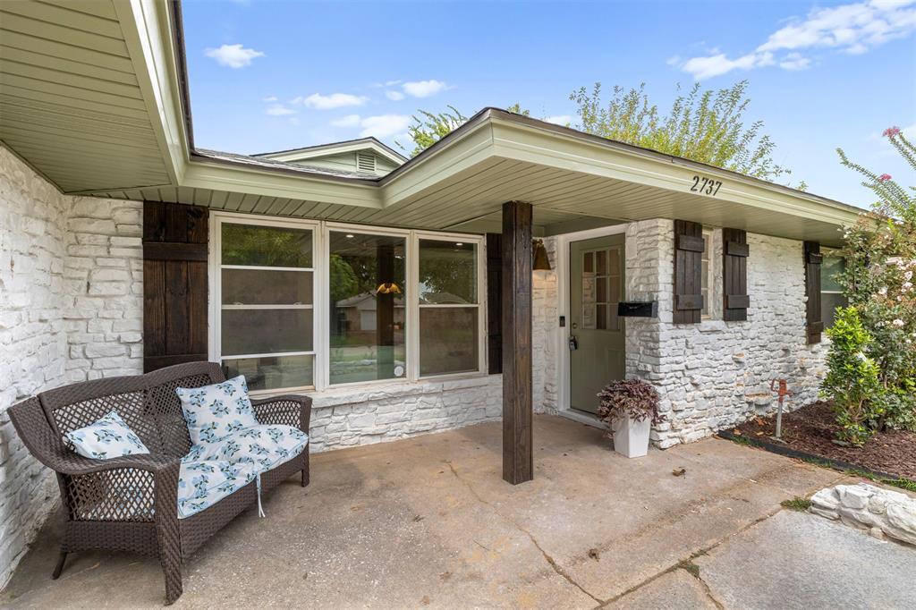 Home front with white stone facade, covered entry, and two patio chairs.