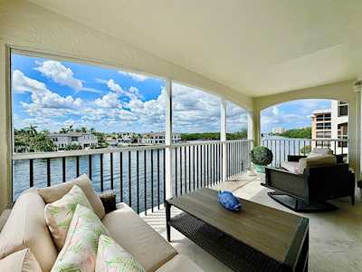 Furnished apartment balcony overlooking a canal, with cushioned seating and a dark coffee table.
