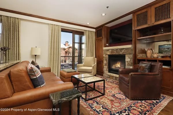Living room with a stone fireplace, wood built-ins, leather seating, and glass doors to a balcony.