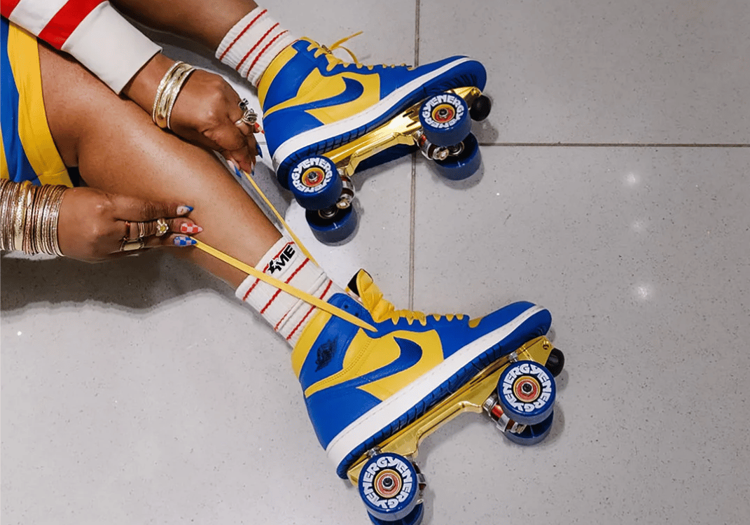 A woman laces bright blue and yellow quad roller skates while seated on a tiled floor.