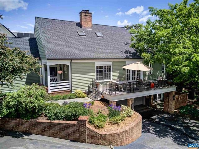 Light green house with a raised patio deck, umbrella, and curved brick garden wall.