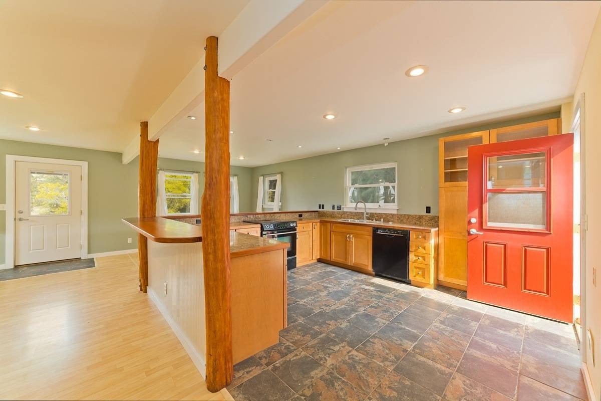 Kitchen with honey-colored cabinets, exposed timber posts, dark tile flooring, and a bright red open door.