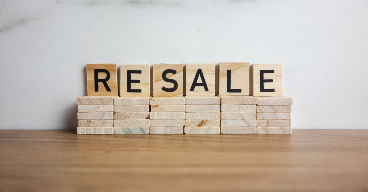Five lettered wooden blocks that spell "RESALE" displayed on top of stacks of wooden blocks and a wooden surface.