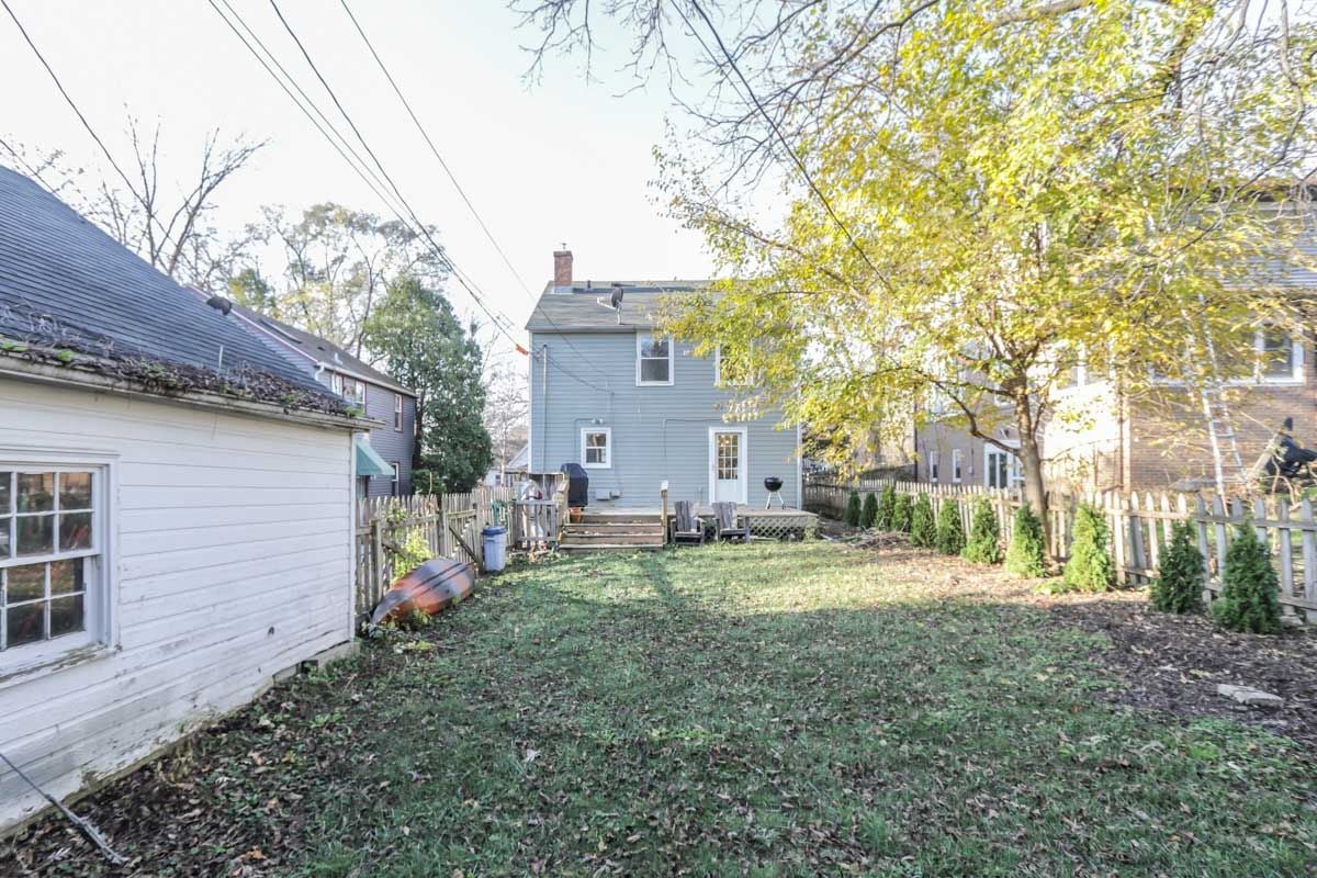 Fenced backyard behind a blue-gray house, with a small deck and a white outbuilding.