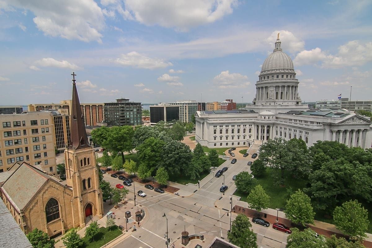 Downtown Madison view featuring the domed State Capitol, leafy trees, and a church.