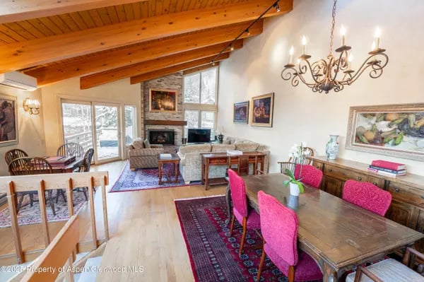Open-plan living and dining room with a vaulted wood ceiling, fireplace, and pink dining chairs.
