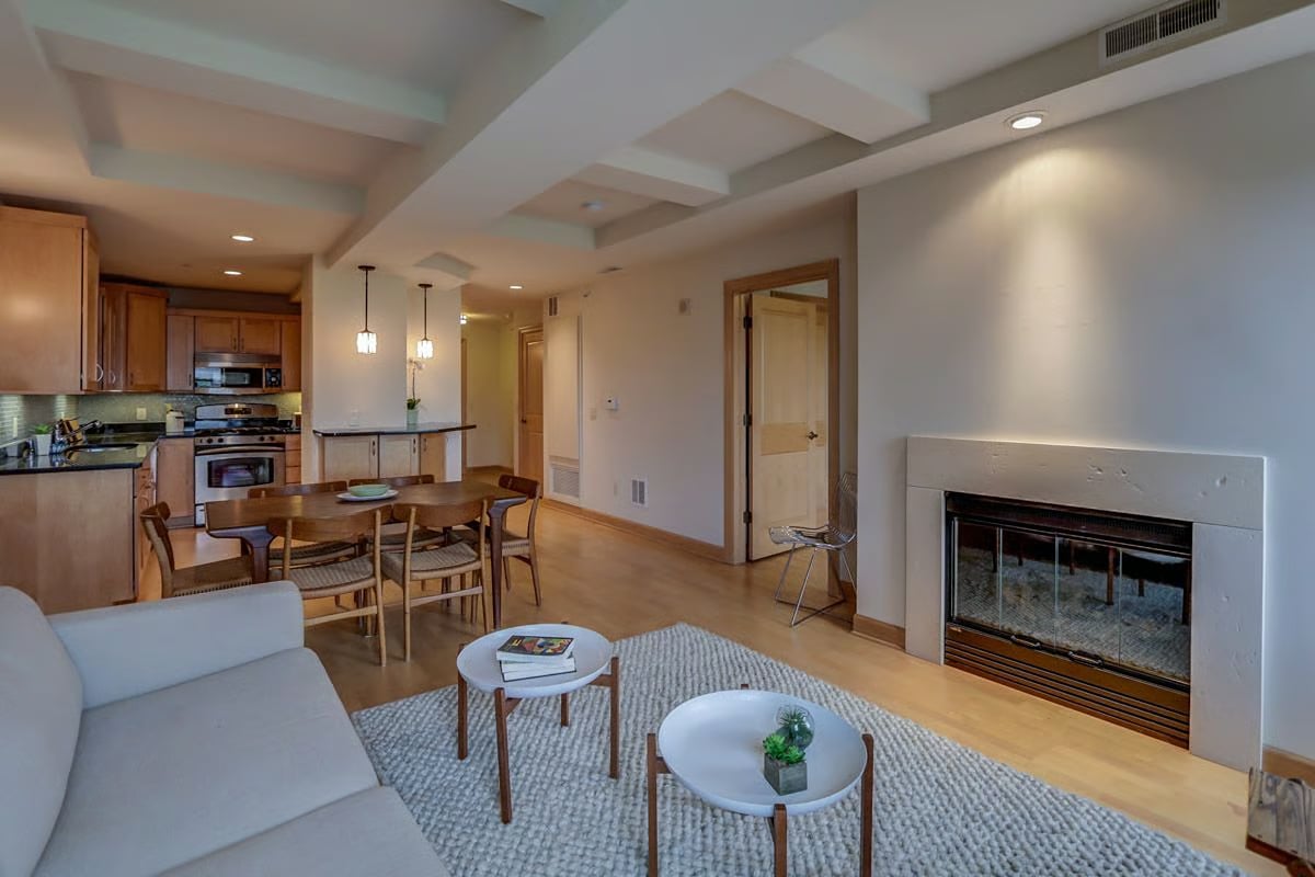 Open-plan living and dining area with a fireplace, coffered ceiling, and wood-cabinet kitchen.