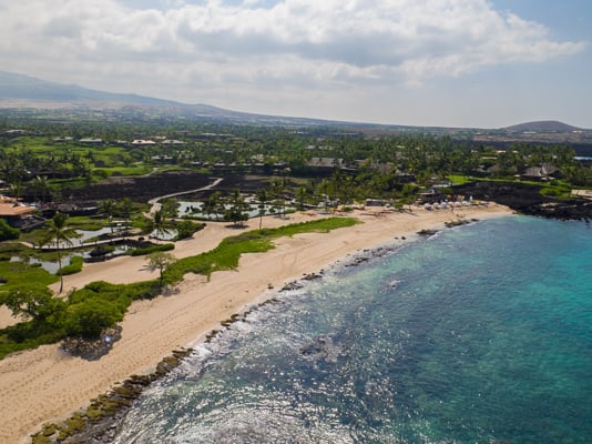 Hawaiian coastline with a sandy beach, turquoise water, and green inland landscape.