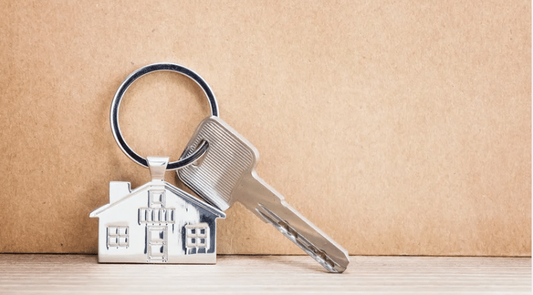 Silver key and house-shaped keychain resting on a light wood surface.