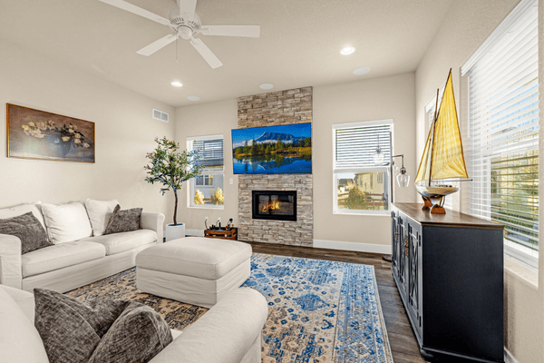 Living room with white sectional sofas, blue patterned rug, and stone fireplace beneath a landscape display.